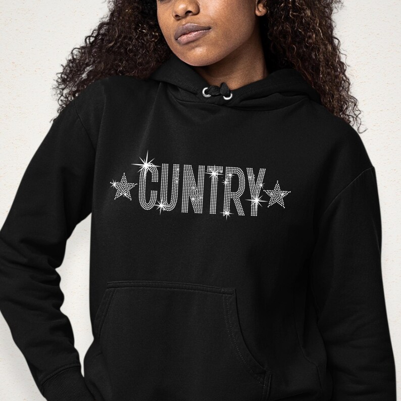May include: Black hoodie with the word "CUNTRY" spelled out in sparkling rhinestones. The word is flanked by rhinestone starbursts. The hoodie has a front pocket and a hood with drawstrings.