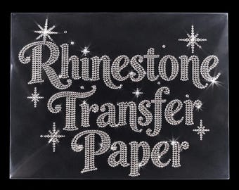 May include: A clear sheet of rhinestone transfer paper featuring the text Rhinestone Transfer Paper in a cursive font, constructed from small, reflective silver-toned rhinestones, accented by several sparkling star-shaped icons.