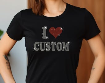Op de afbeelding: Zwart T-shirt met een strass-ontwerp dat "Ik hou van maatwerk" zegt met een rood strass-hart.