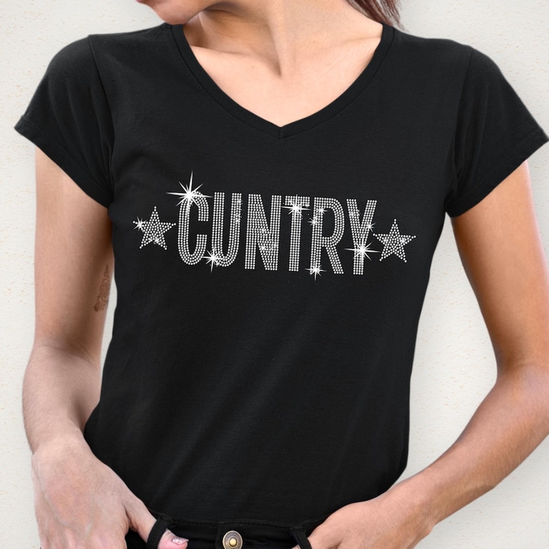May include: Black V-neck t-shirt with the word "CUNTRY" spelled out in sparkling rhinestones. The word is flanked by starburst designs. The shirt is a short-sleeved style.