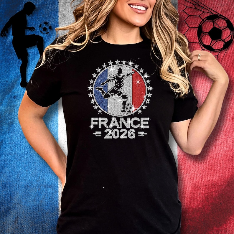 May include: Black Bella Canvas unisex t-shirt featuring a rhinestone “France 2026” soccer design. The artwork includes a soccer player silhouette layered over a French flag inspired background with sparkling star accents surrounding the circular design. Royal blue, red, and silver rhinestones are used throughout the graphic. The model is wearing a black short sleeve t-shirt.