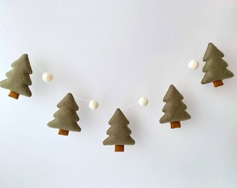 May include: A festive garland featuring felt Christmas trees in olive green with brown trunks, interspersed with white felt balls. The trees are strung on a thin white string, creating a charming holiday decoration.