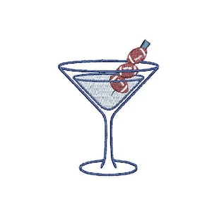 May include: A blue embroidered martini glass with a football garnish. The glass is filled with a textured blue liquid and has a stem. Three miniature footballs are skewered on a toothpick.