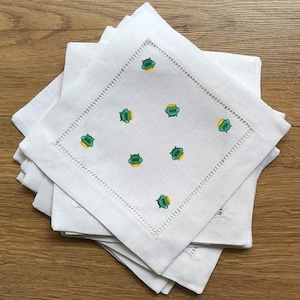 May include: A stack of white linen napkins with a green and yellow embroidered pot of gold design.