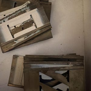 Könnte beinhalten: Eine Sammlung verwitterter, rechteckiger Metallschablonen mit ausgeschnittenen Buchstaben. Die Schablonen haben eine angelaufene, bräunlich-graue Patina mit sichtbaren Altersspuren, Abnutzungserscheinungen und weißen Farbresten.