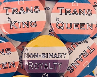 May include: A collection of colorful button pins with different designs and text. The pins feature a crown and the words "Trans King", "Trans Queen", and "Non-Binary Royalty".