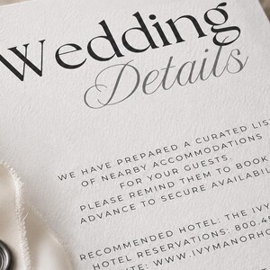 May include: A white card with black text reading Wedding Details, followed by information about nearby accommodations, a recommended hotel, and contact details. The card features a textured surface and a dark grey wax seal in the corner.