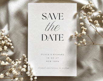 May include: A rectangular white card with black text reading SAVE the DATE, OLIVIA & RICHARD, 18.09.27, NEW YORK, and formal invitation to follow. The card is surrounded by small white dried flowers on a textured off-white fabric surface.