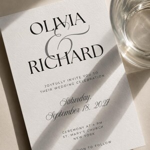 May include: A white wedding invitation card with black serif and script typography. The text reads: OLIVIA & RICHARD, JOYFULLY INVITE YOU TO THEIR WEDDING CELEBRATION, Saturday, September 18, 2027, CEREMONY AT 4 PM, ST. MARY'S CHURCH, NEW YORK, RECEPTION TO FOLLOW.