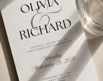 Puede incluir: Una tarjeta de invitación de boda blanca con tipografía negra con serifa y cursiva. El texto dice: OLIVIA & RICHARD, JOYFULLY INVITE YOU TO THEIR WEDDING CELEBRATION, Saturday, September 18, 2027, CEREMONY AT 4 PM, ST. MARY'S CHURCH, NEW YORK, RECEPTION TO FOLLOW.