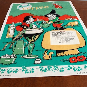 May include: A vintage Irish coffee tea towel with a green background and a whimsical illustration. The design includes leprechauns, a recipe, and the words "Irish Coffee". The towel is made of a linen blend.