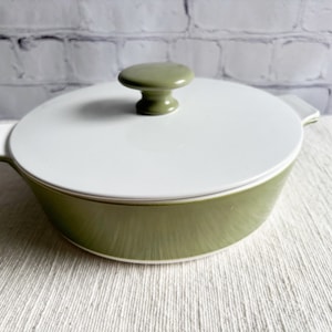 Peut inclure: Un plat à gratin en céramique vert et blanc avec un couvercle et un bouton sur le dessus. Le plat est rond et a un intérieur blanc.