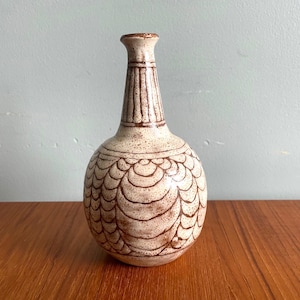 May include: A white ceramic vase with a brown geometric pattern. The vase has a round body and a narrow neck.