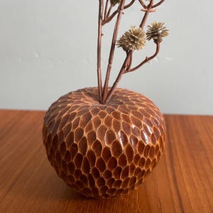 May include: A small, brown, ceramic vase with a textured, honeycomb-like surface. The vase is filled with dried flowers.
