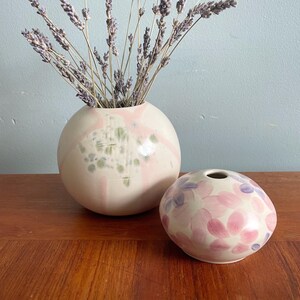Peut inclure: Deux vases en céramique, l'un avec un glaçage moucheté rose et blanc et l'autre avec un motif floral rose et blanc. Les deux vases sont posés sur une surface en bois.