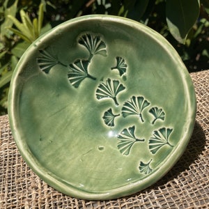 May include: A small, green ceramic bowl with a raised design of ginkgo leaves. The bowl is perfect for holding small items like jewelry or keys.