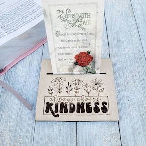 May include: Wooden sign with the text "always choose kindness" in a decorative font. The sign is decorated with a floral design and a small card with a poem about the strength of love.