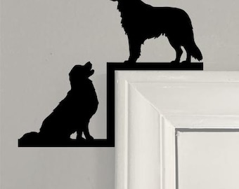 May include: Black silhouette of two dogs, one standing and one sitting, on a white wall. The dogs are positioned on a black, L-shaped frame, creating a decorative accent. The dogs are facing each other.