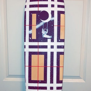 May include: A longboard skateboard with black and white checkered pattern and red lines. The deck features a space-themed design with an astronaut on a swing in front of a crescent moon and stars. The skateboard has black trucks and brown wheels with the word "BEBO" printed on the trucks.