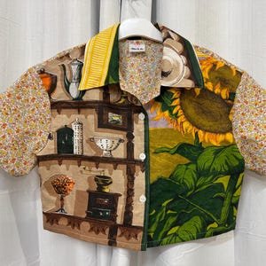 May include: A short-sleeved button-up shirt with a unique patchwork design. One side features a sunflower print, while the other showcases a kitchen scene. The sleeves have a floral pattern, and the collar has a yellow stripe.