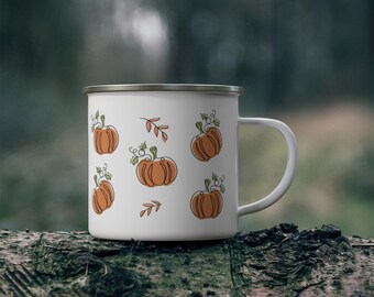 Puede incluir: Taza de esmalte blanco con borde plateado, decorada con calabazas naranjas y vides verdes. La taza tiene un asa blanca. El diseño se repite alrededor de la taza, ideal para la decoración con temática otoñal.