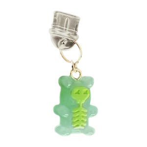 Könnte beinhalten: Ein silberfarbener Charm mit einem goldfarbenen Ring und einem grünen Gummibären-Anhänger. Der Gummibär hat ein grünes Alien-Skelett-Design in der Mitte. Der Charm ist an einem silberfarbenen Verschluss befestigt.