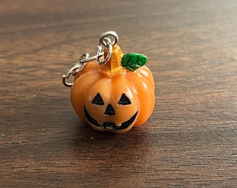Puede incluir: Un pequeño dije de calabaza naranja con una cara sonriente, ojos negros y boca negra. La calabaza tiene una hoja verde y un accesorio de llavero plateado. Este dije temático de Halloween es un accesorio festivo.