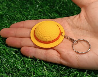 Puede incluir: Un llavero con forma de sombrero de paja amarillo y naranja con un anillo de metal plateado.