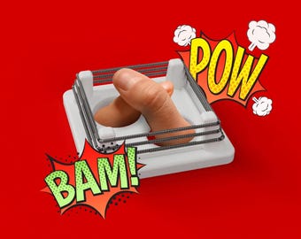 Puede incluir: Un ring de boxeo de plástico blanco con dos dedos dentro, un dedo está doblado en el nudillo. Las palabras "BAM!" y "POW!" están en bocadillos de diálogo de estilo cómic.