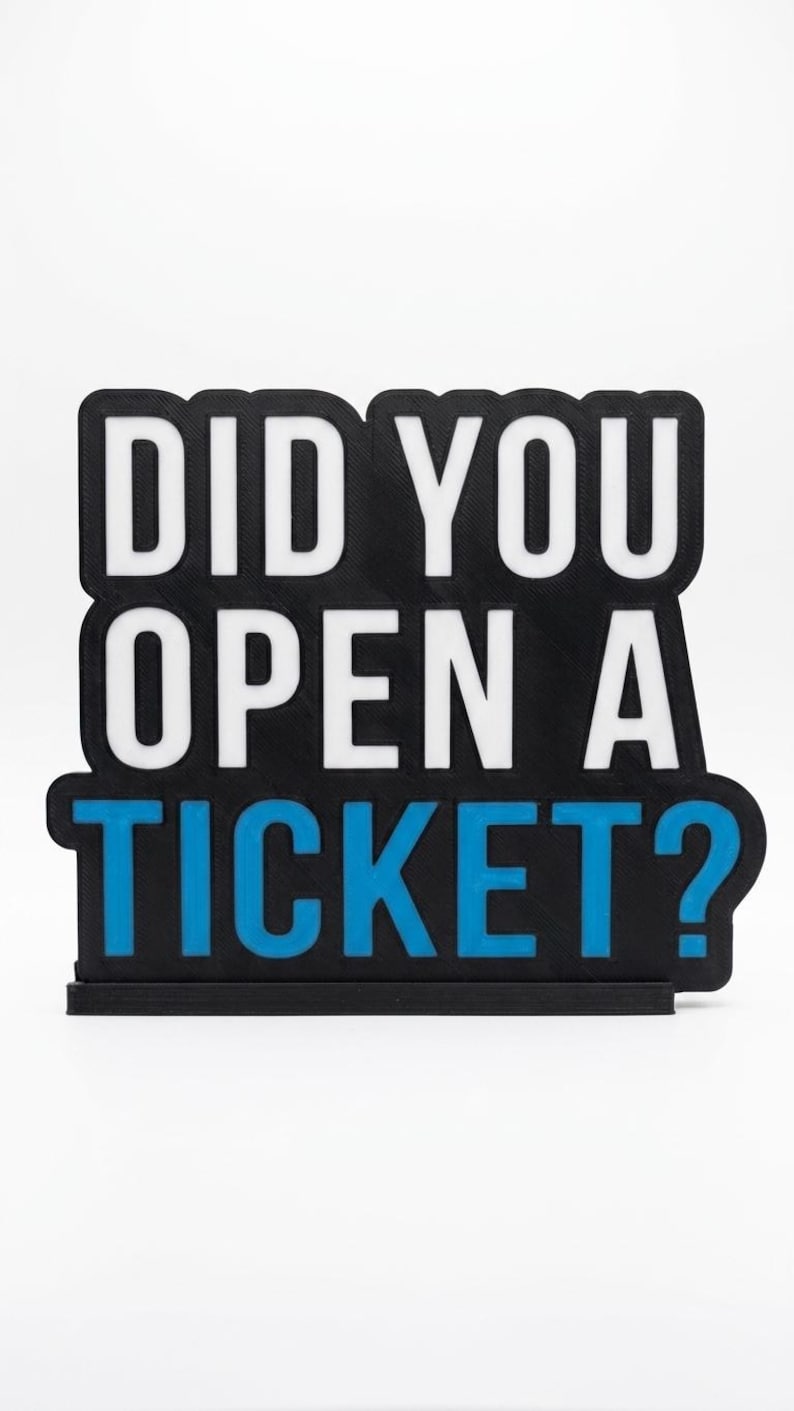 Puede incluir: Un letrero negro con el texto "DID YOU OPEN A TICKET?" en blanco y azul. El letrero es rectangular con esquinas redondeadas y se asienta sobre una peque&ntilde;a base negra. El texto est&aacute; en negrita, sin serifa.
