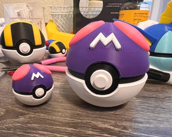 Könnte beinhalten: Drei Pokébälle, einer lila mit einem weißen M, einer weiß mit einem schwarzen Ring und einem weißen Knopf und einer blau mit einem weißen Flügel.