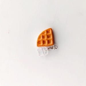 May include: A small, brown waffle charm with a silver chain and a clear plastic charm attached.