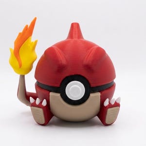 Puede incluir: Figura Pokémon roja y marrón impresa en 3D, sosteniendo una llama amarilla y naranja. La figura tiene una banda negra en el medio y detalles blancos. El personaje está sentado.