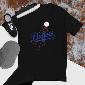 Puede incluir: Camiseta negra con un gráfico azul y rojo de una pelota de béisbol con la palabra "Duffers" en una fuente azul de escritura.