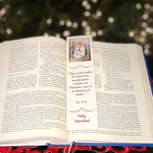 May include: A bookmark with a religious image of a baby Jesus in a manger. The bookmark is white with gold trim and has the text "Hoy, en la ciudad de David, ha nacido para ustedes un Salvador, que es el Mesías y el Señor."  Luke 2:11. The bookmark also has the text "Feliz Navidad" at the bottom.