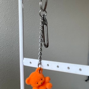 Op de afbeelding: Oranje pluche teddybeer sleutelhanger met een zilveren ketting en een zilveren haak.