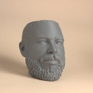 May include: A gray 3D printed bust of a person's head with a beard and a detailed design on the forehead.