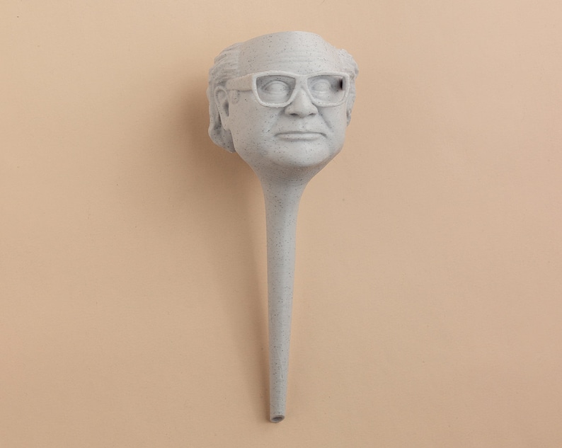 May include: A white ceramic sculpture of a person's head with glasses. The sculpture is attached to a long, thin, white stem.