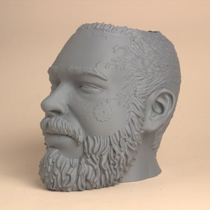 May include: A gray 3D printed sculpture of a man's head with a beard and tattoos. The head is tilted to the side and the man's eyes are closed.