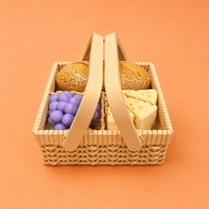 May include: A wicker picnic basket filled with food items. The basket contains two round bread rolls, a bunch of purple grapes, and several cheese wedges. The basket has a wooden handle and is set against an orange background.