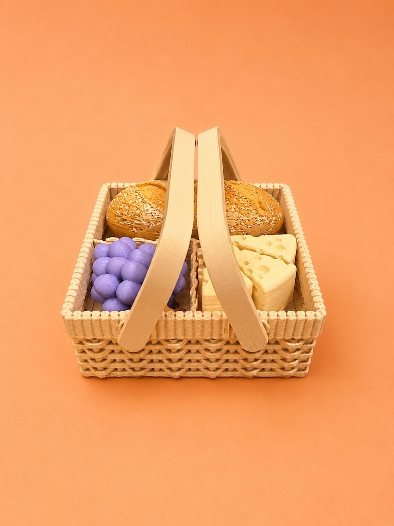 May include: A wicker picnic basket filled with food items. The basket contains two round bread rolls, a bunch of purple grapes, and several cheese wedges. The basket has a wooden handle and is set against an orange background.