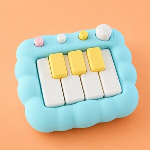 May include: A light blue toy piano with a cloud-shaped frame. The piano has white and yellow keys, and pink, white, and yellow buttons. A white knob is on the right side of the piano. The background is a solid orange color.