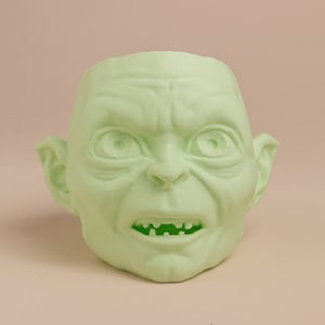 May include: A green 3D printed sculpture of a goblin's head with a wide open mouth and visible teeth.