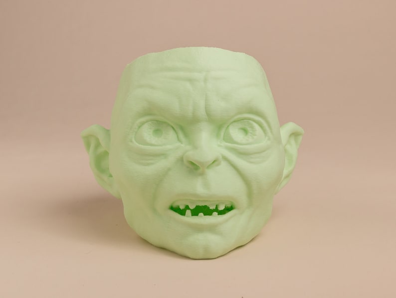 May include: A green 3D printed sculpture of a goblin's head with a wide open mouth and visible teeth.
