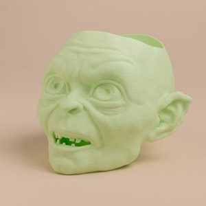 May include: A green plastic planter shaped like the head of Gollum from the Lord of the Rings. The planter has a hole in the top for planting.