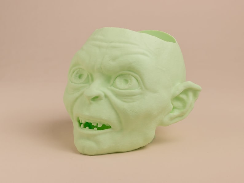 May include: A green plastic planter shaped like the head of Gollum from the Lord of the Rings. The planter has a hole in the top for planting.