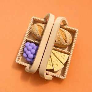 May include: A wicker basket with a handle, containing two loaves of bread, a bunch of purple grapes, and three slices of yellow cheese. The basket is set against an orange background.