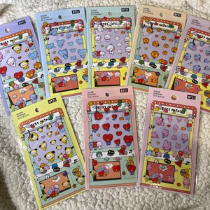 May include: A collection of BT21 Mini clear stickers in various pastel colors. Each package features a different assortment of cartoon character stickers, with the BT21 logo and "Clear Sticker BT21 Mini" text. The stickers are displayed on a white, textured surface.