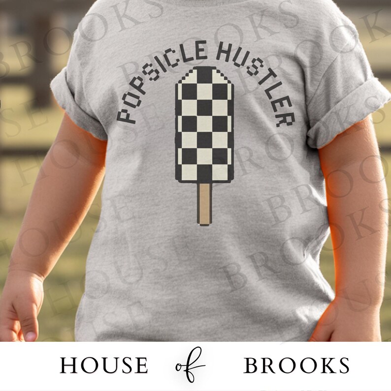 May include: A light gray t-shirt featuring the text "POPSICLE HUSTLER" arched above a pixelated popsicle design with a black and white checkered pattern. The popsicle is on a brown stick.