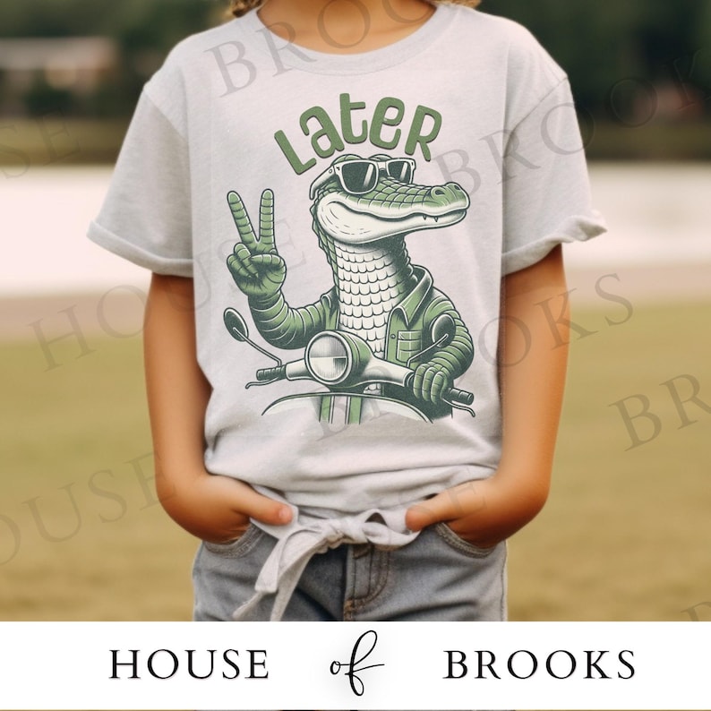May include: A light gray t-shirt with a green alligator wearing sunglasses and riding a scooter. The alligator is giving a peace sign and the text "Later" is above the alligator.